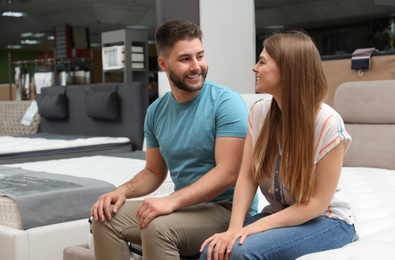 Photo of Happy couple sitting on new orthopedic mattress in store