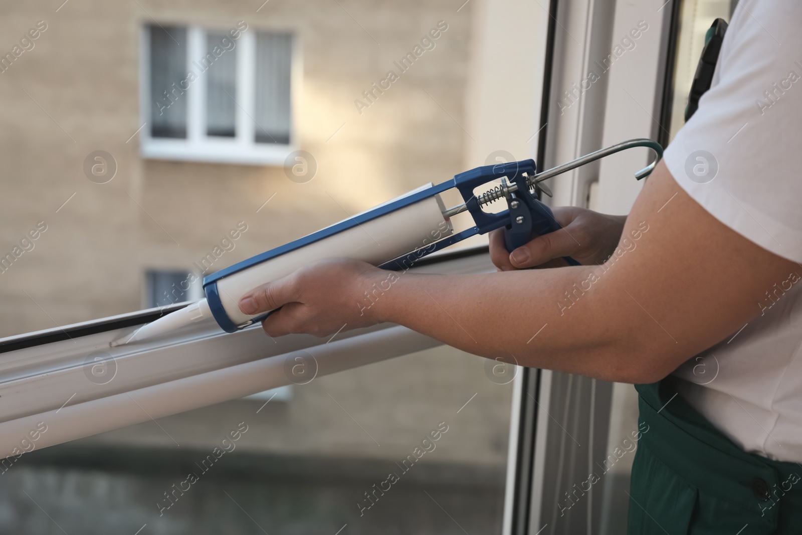 Photo of Construction worker sealing window with caulk indoors, closeup