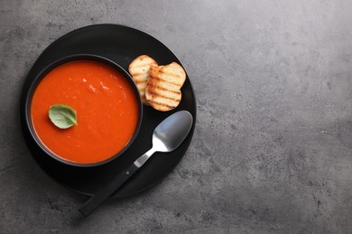 Photo of Delicious tomato cream soup in bowl and pieces of grilled bread served on dark textured table, top view. Space for text