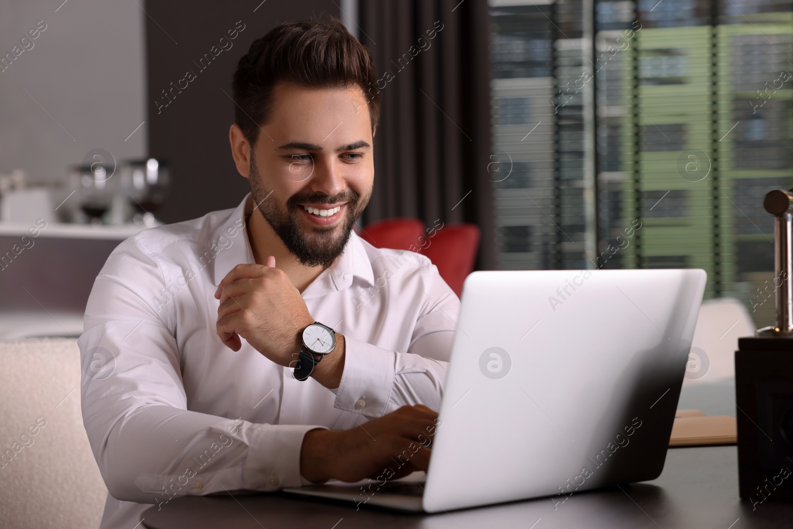 Photo of Happy young man working on laptop at table in office