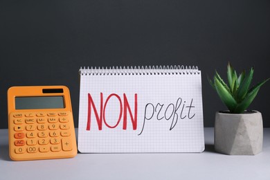 Photo of Notebook with phrase Non Profit, calculator and houseplant on white table