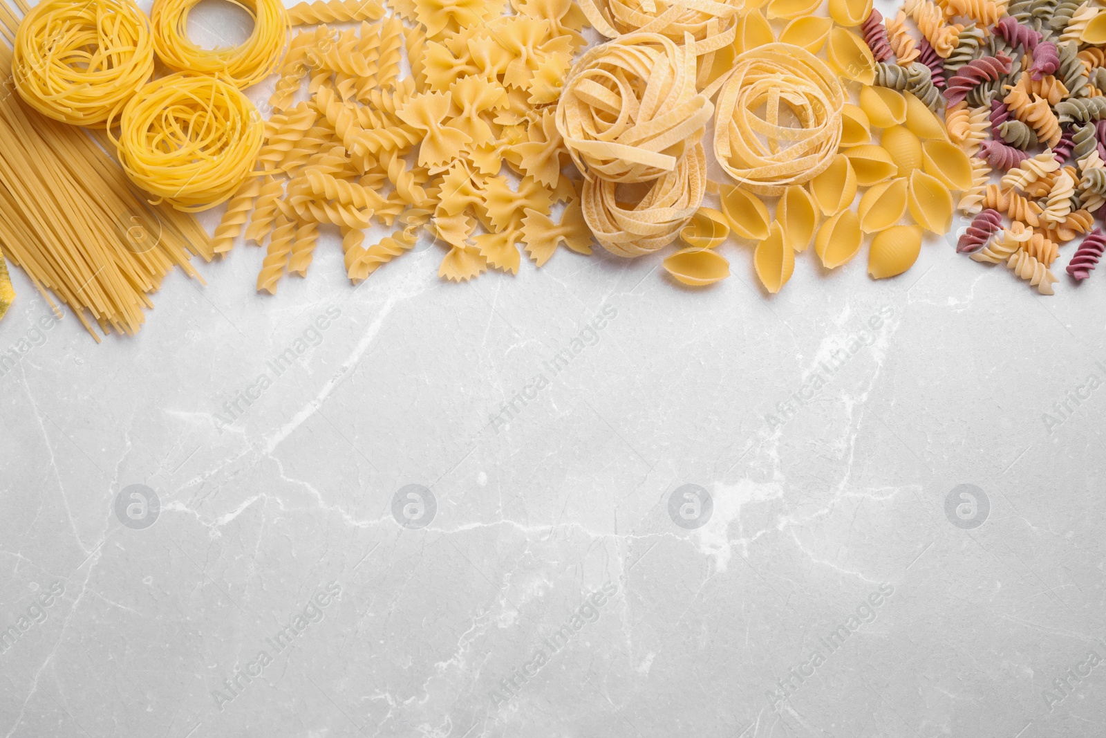 Photo of Different types of pasta on light grey marble table, flat lay. Space for text