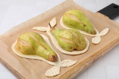 Photo of Board with raw dough and fresh pears on white tiled table, closeup