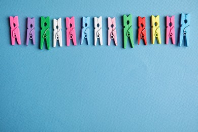 Photo of Many colorful wooden clothespins on light blue background, flat lay. Space for text