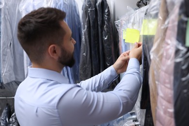 Dry-cleaning service. Worker sticking paper note onto clothes indoors