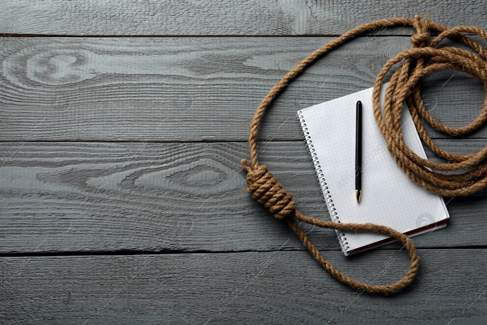 Photo of Rope noose and blank notebook with pen on grey wooden table, flat lay. Space for text