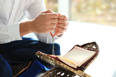 Photo of Muslim man with Koran and misbaha praying indoors, closeup