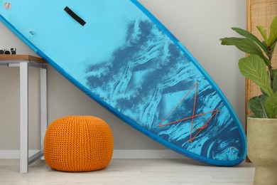 SUP board, orange pouf and houseplant in room. Interior element