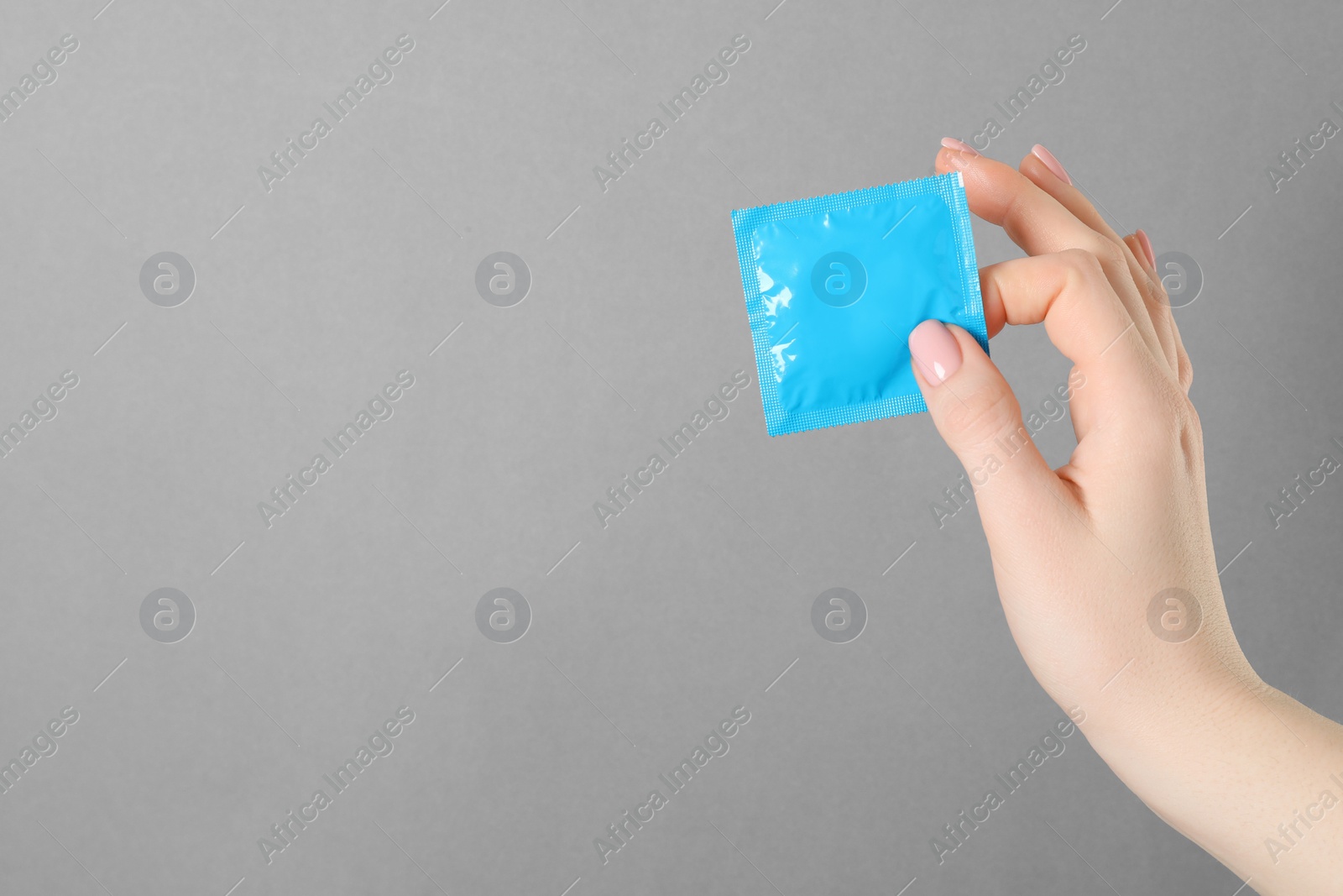 Photo of Woman holding condom on grey background, closeup. Space for text