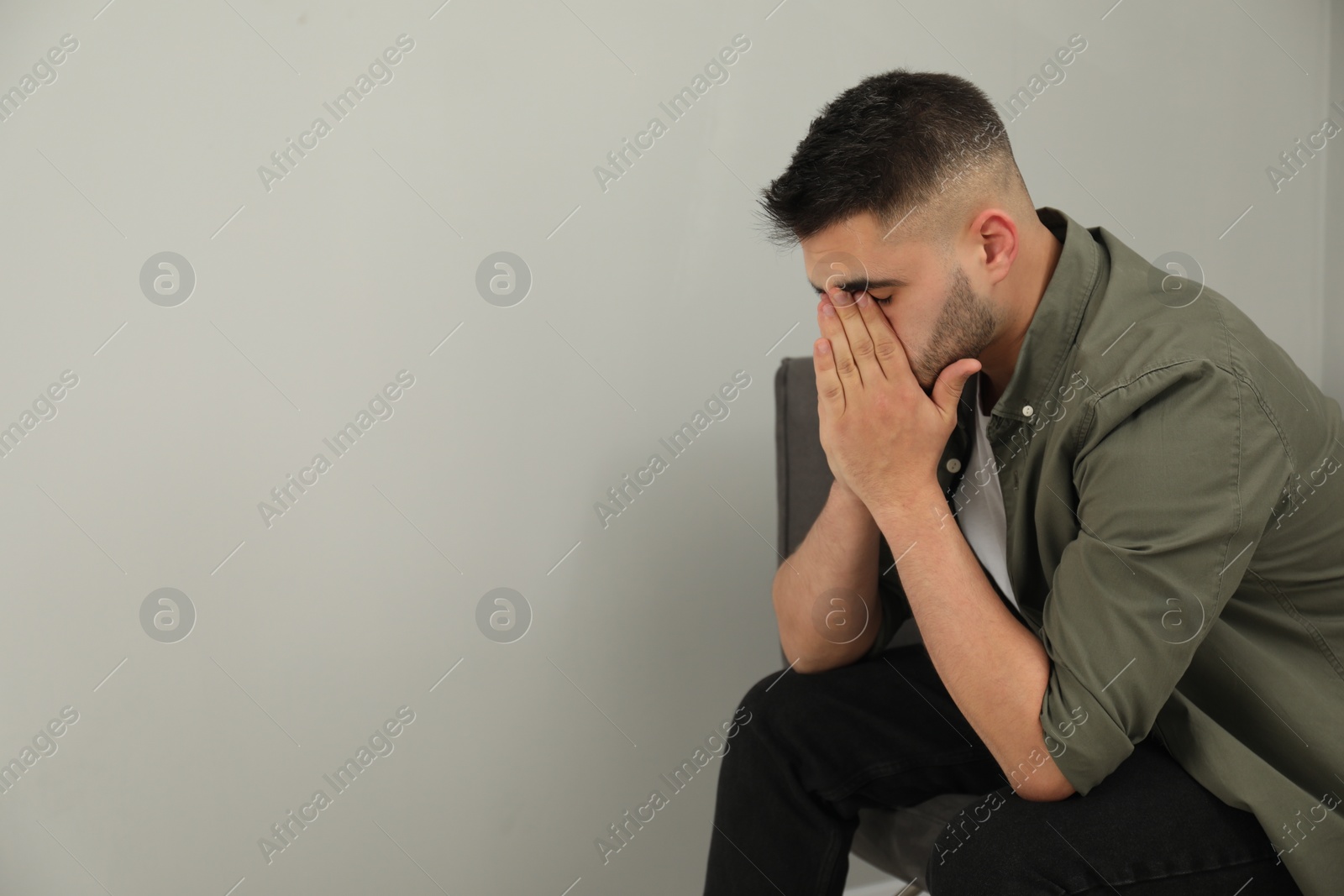 Photo of Sad man covering face with hands near light grey wall. Space for text