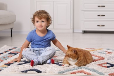 Photo of Little boy and cute ginger cat on carpet at home