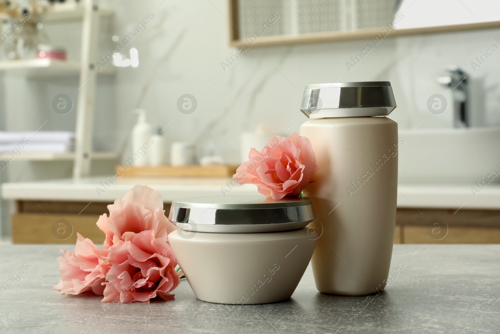 Photo of Hair care cosmetic products and beautiful flowers on light grey table in bathroom