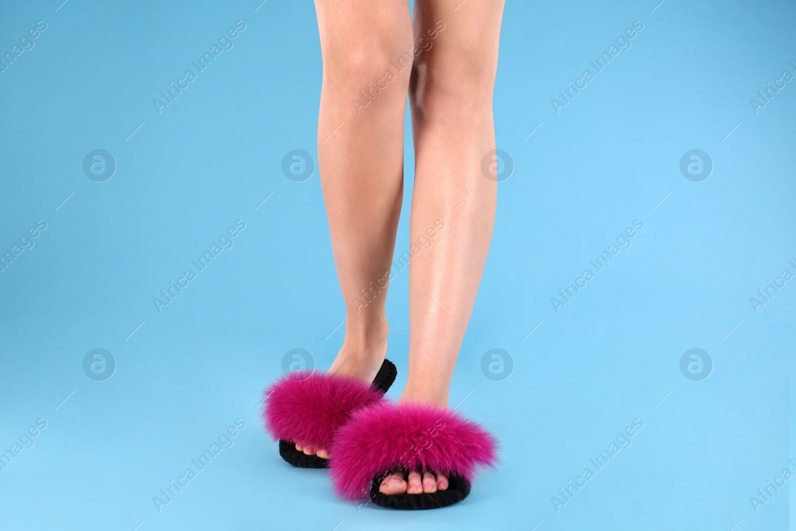 Photo of Woman in fluffy slippers on light blue background, closeup