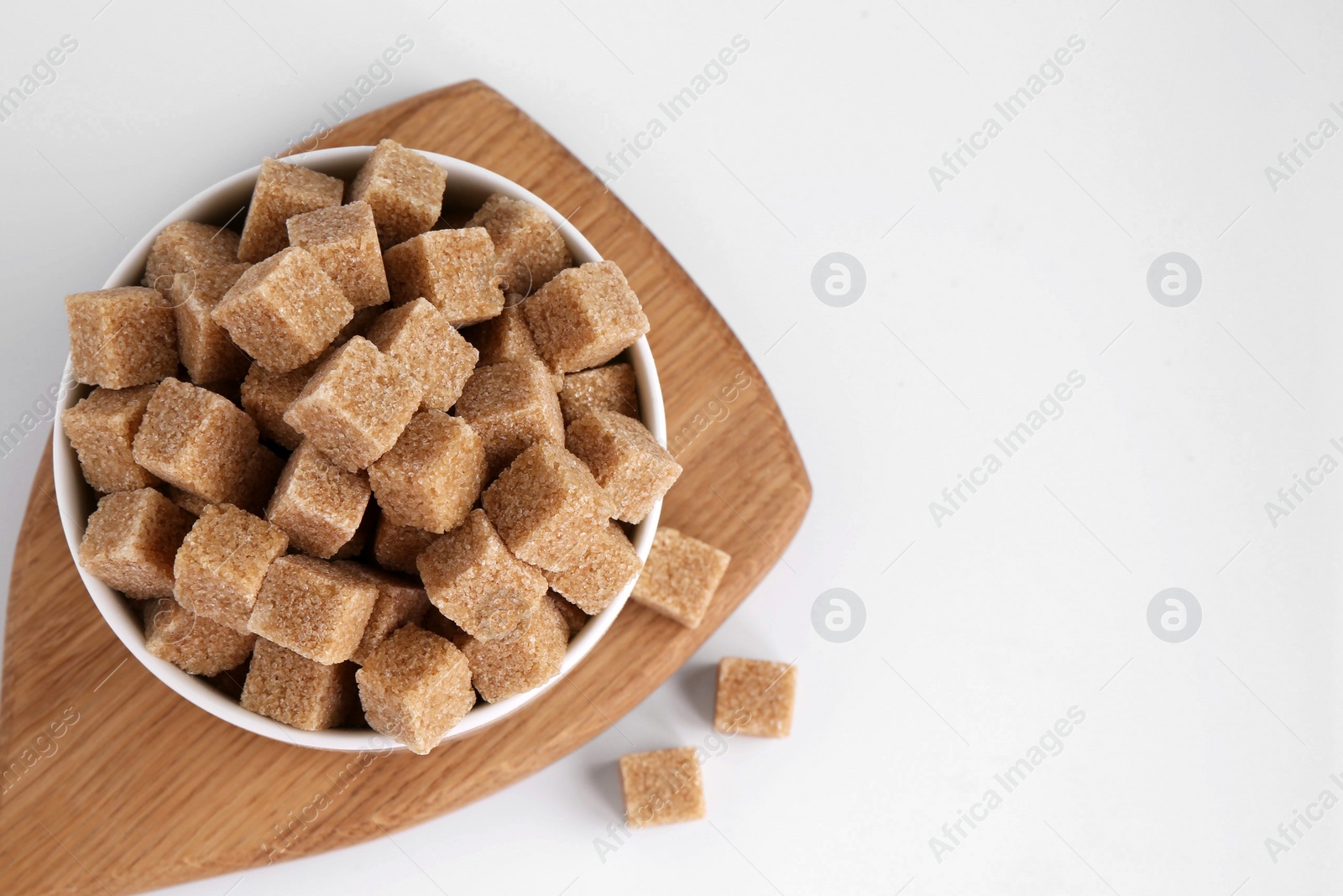 Photo of Brown sugar cubes in bowl on white background, top view. Space for text