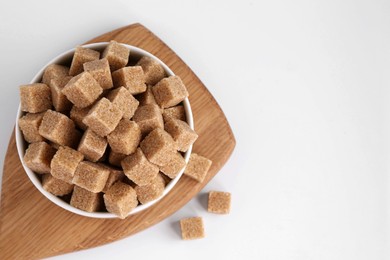 Photo of Brown sugar cubes in bowl on white background, top view. Space for text