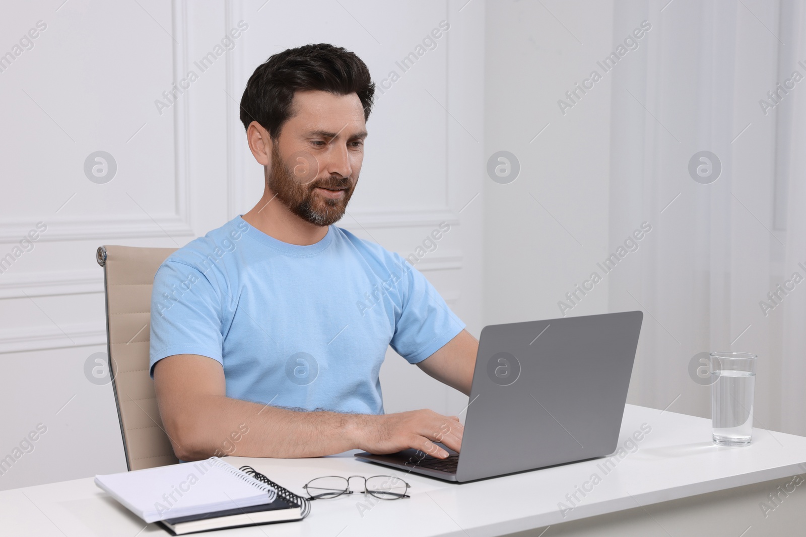 Photo of Man using laptop at white table indoors