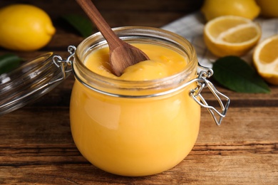 Photo of Delicious lemon curd in glass jar on wooden table