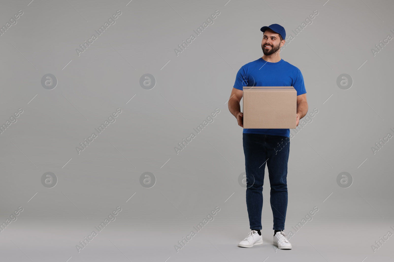 Photo of Happy young courier with parcel on grey background, space for text