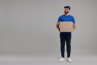 Happy young courier with parcel on grey background, space for text