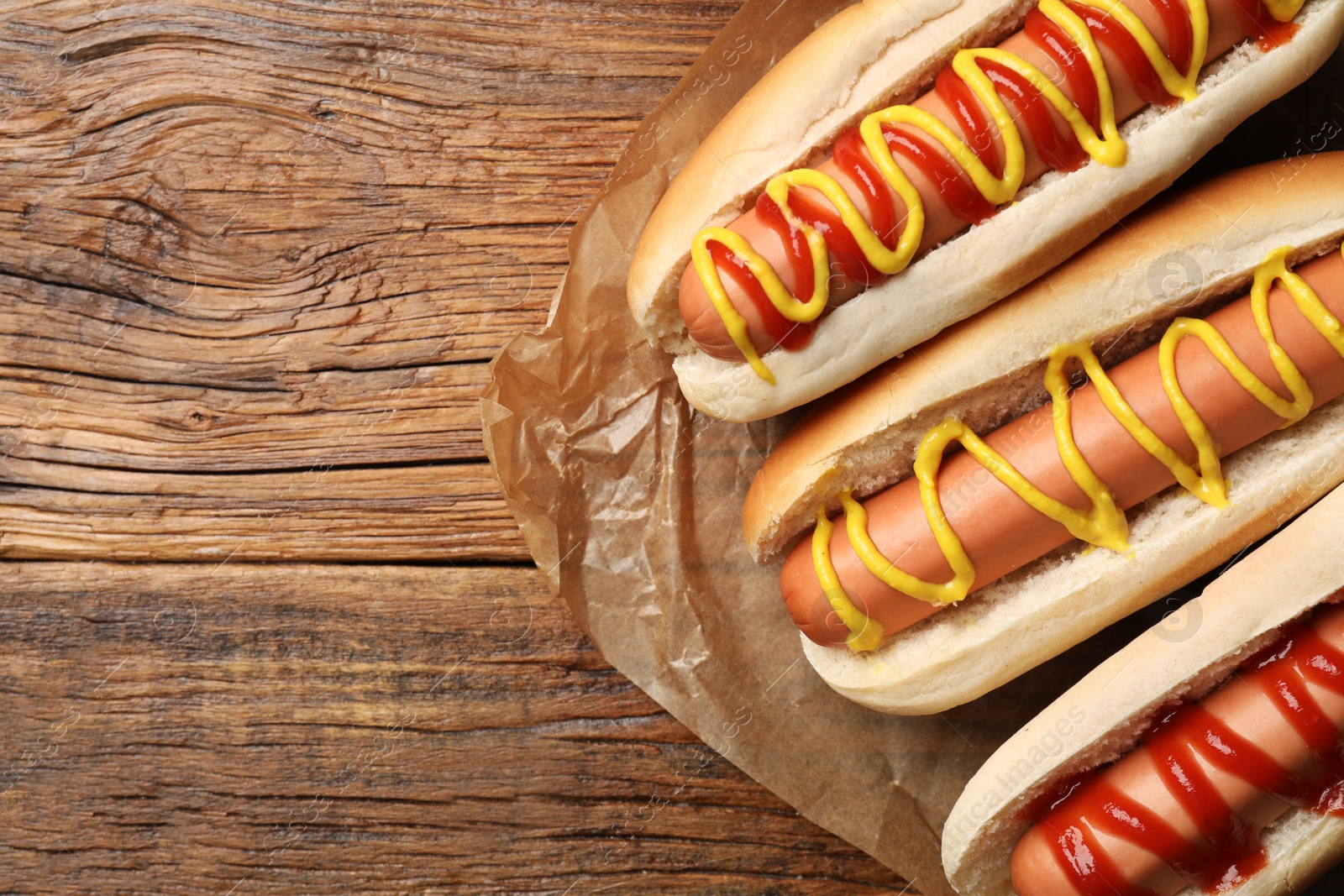 Photo of Delicious hot dogs with mustard and ketchup on wooden table, top view. Space for text