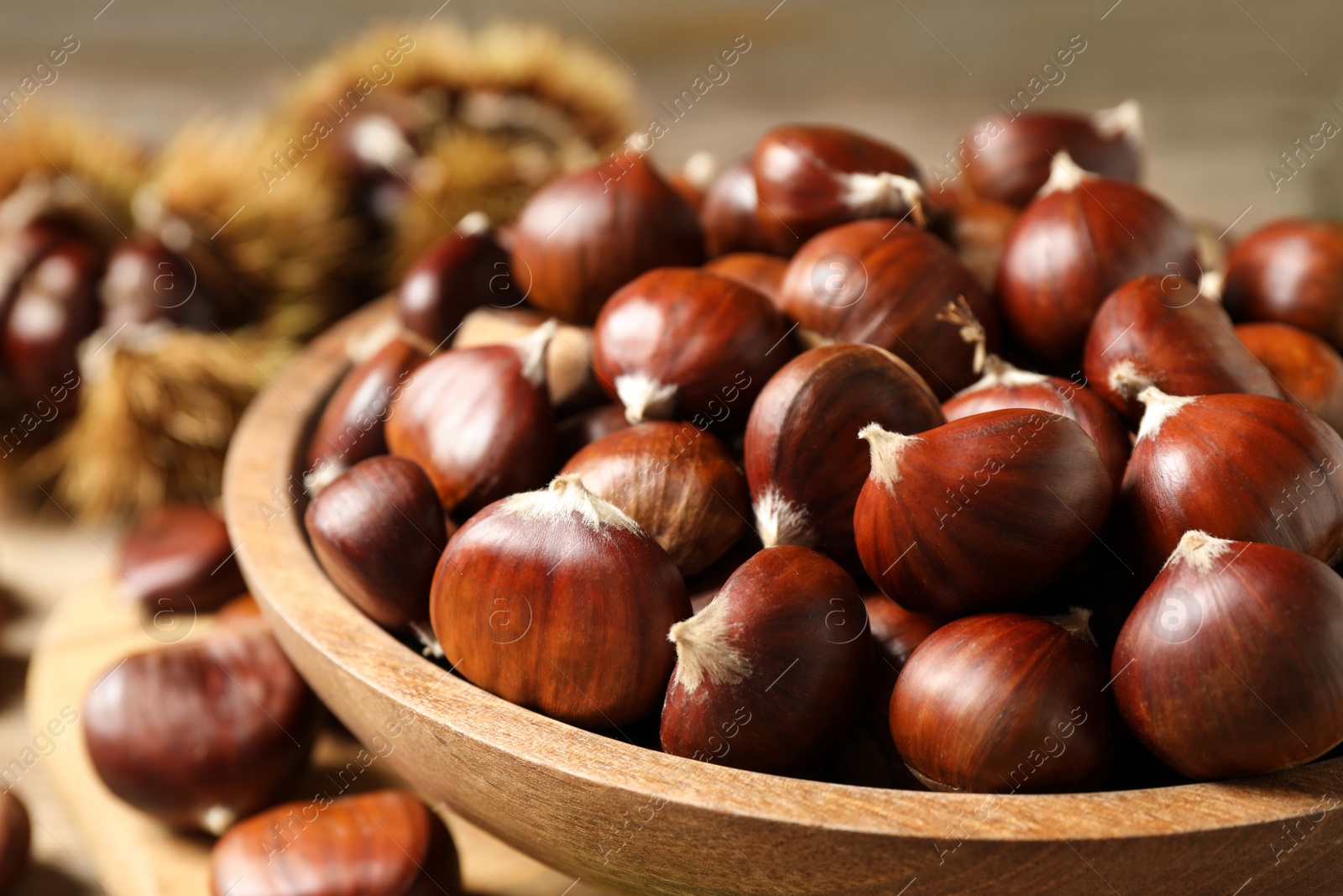 Photo of Fresh sweet edible chestnuts in wooden bowl on table, closeup