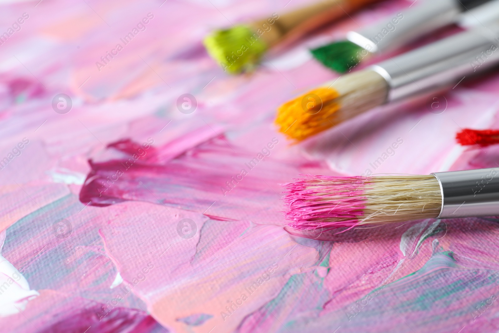 Photo of Set of different brushes on abstract colorful paint, closeup