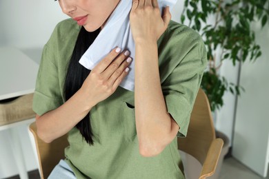 Photo of Young woman using heating pad on neck at home, closeup
