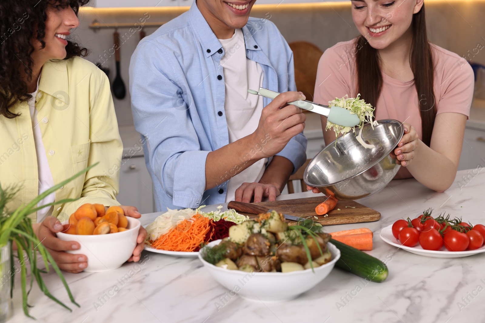 Photo of Friends cooking healthy vegetarian meal at white marble table in kitchen, closeup