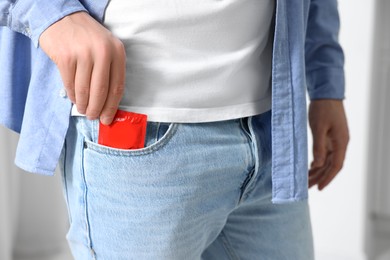 Photo of Man pulling condom out of pocket on blurred background, closeup