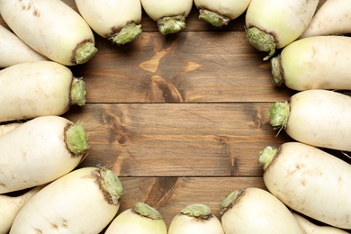 Photo of Frame of white turnips on wooden table, flat lay. Space for text