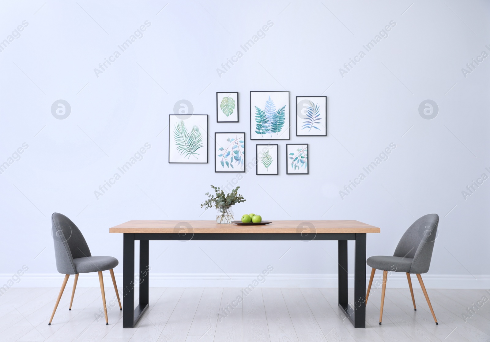 Photo of Stylish room interior with modern table, chairs and paintings of tropical leaves. Idea for design