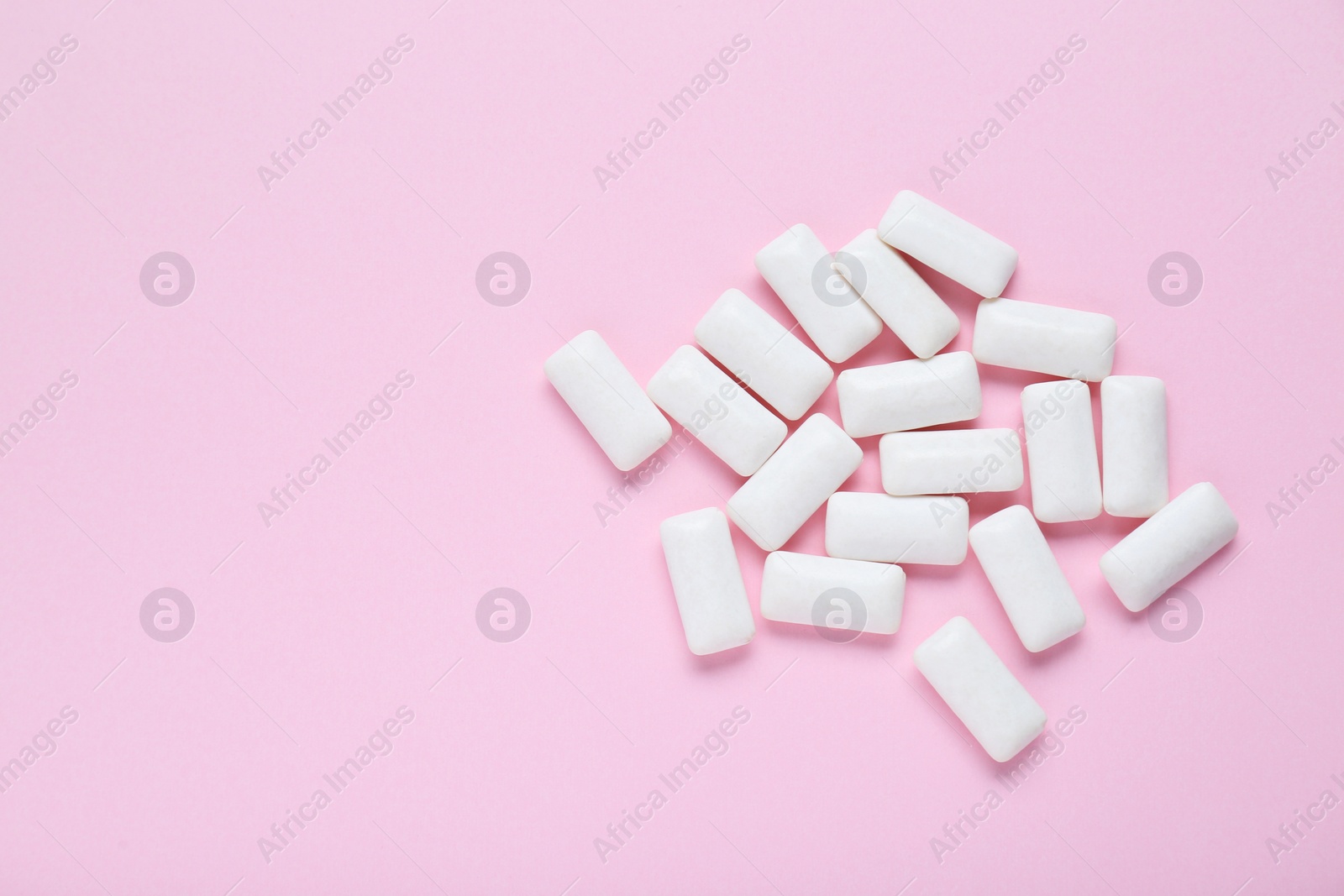 Photo of Tasty white chewing gums on pale pink background, flat lay. Space for text