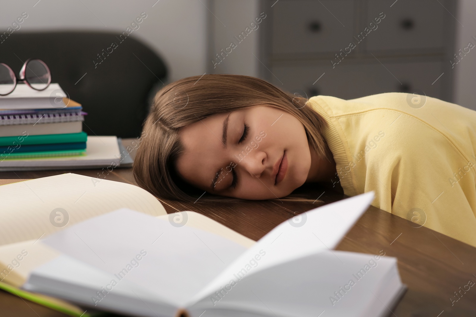 Photo of Young tired woman sleeping near books at wooden table indoors