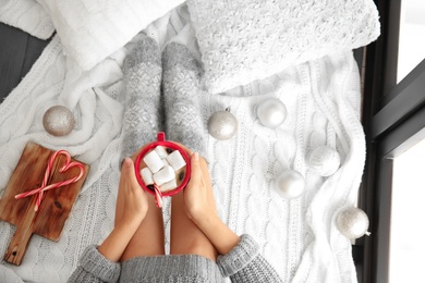 Photo of Woman relaxing with cup of hot winter drink on knitted plaid, top view. Cozy season