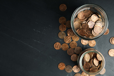 Photo of Glass jars with coins on black table, flat lay. Space for text