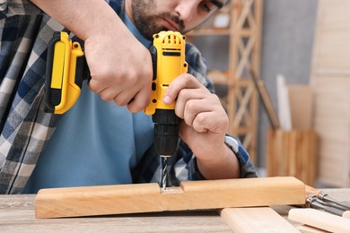 Young handyman working with electric drill at table in workshop, closeup