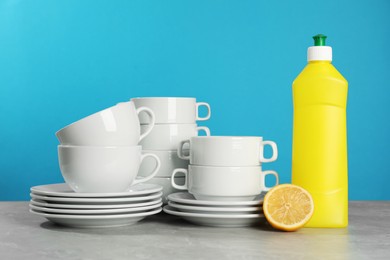 Photo of Clean tableware, dish detergent and lemon on grey table against light blue background