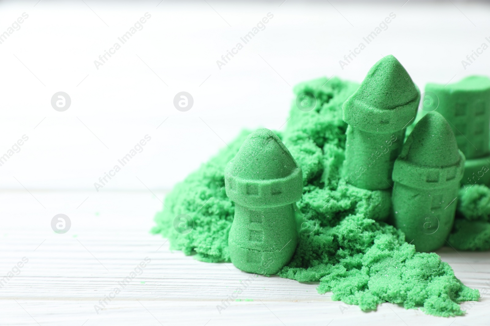 Photo of Castle figures made of green kinetic sand on white wooden table, closeup. Space for text