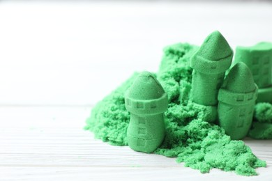 Photo of Castle figures made of green kinetic sand on white wooden table, closeup. Space for text