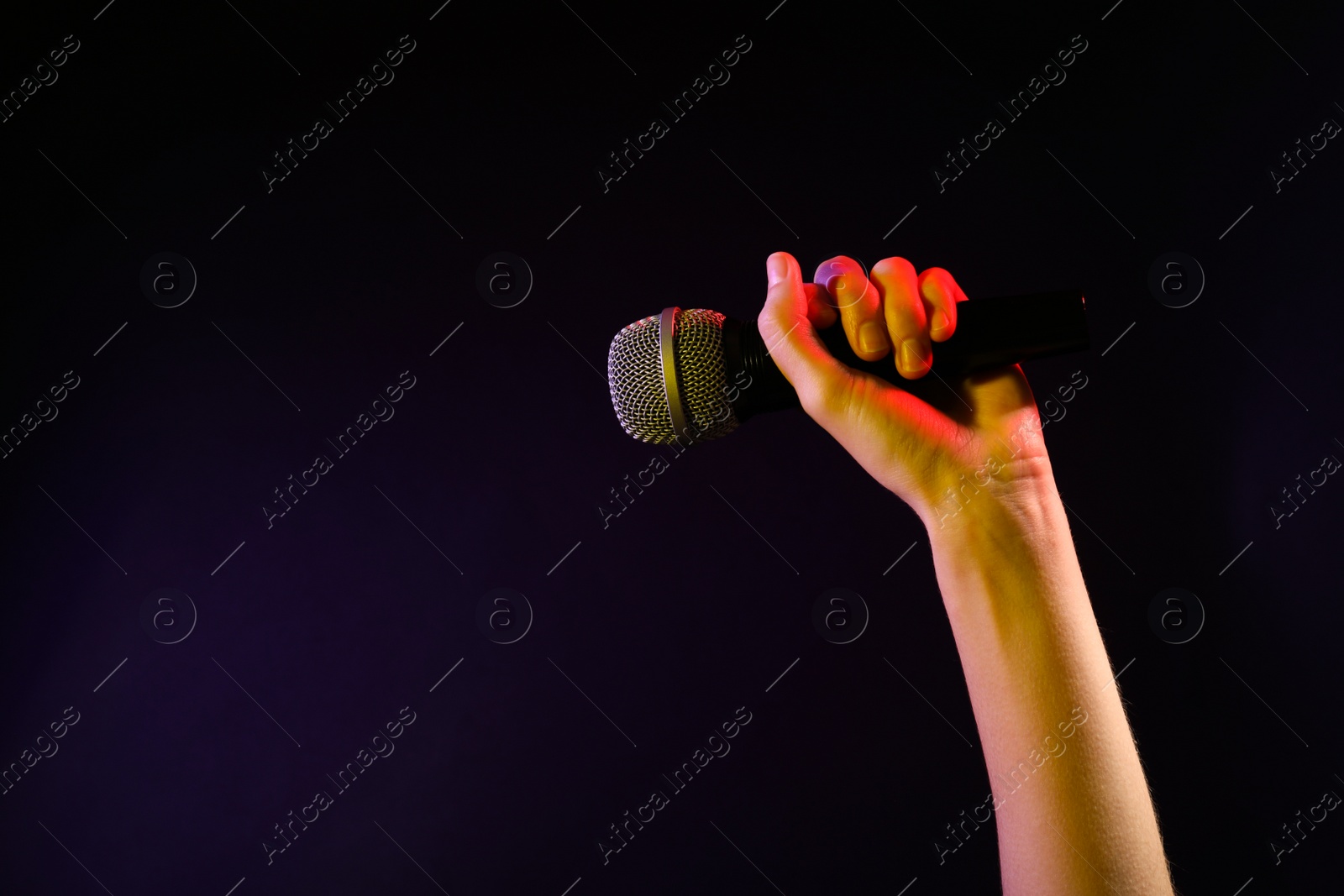 Photo of Woman holding microphone on black background, closeup. Space for text