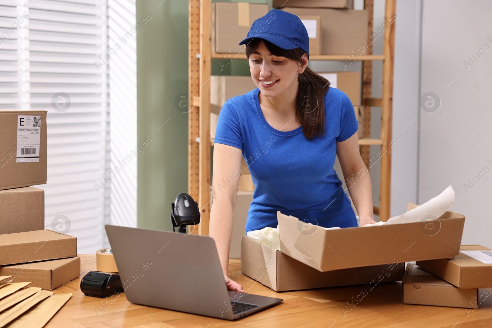 Photo of Parcel packing. Post office worker using laptop at wooden table indoors