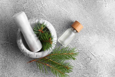 Bottle of aromatic essential oil and mortar with pine branch on light grey table, flat lay