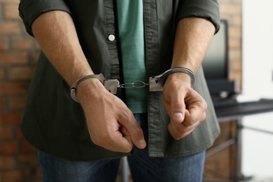 Man detained in handcuffs indoors, closeup view. Criminal law