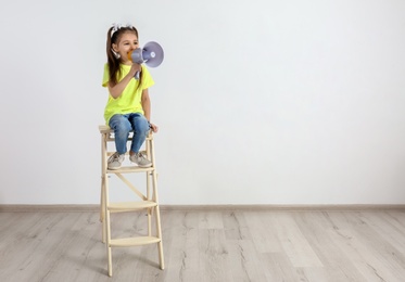 Photo of Cute little girl sitting with megaphone near white wall