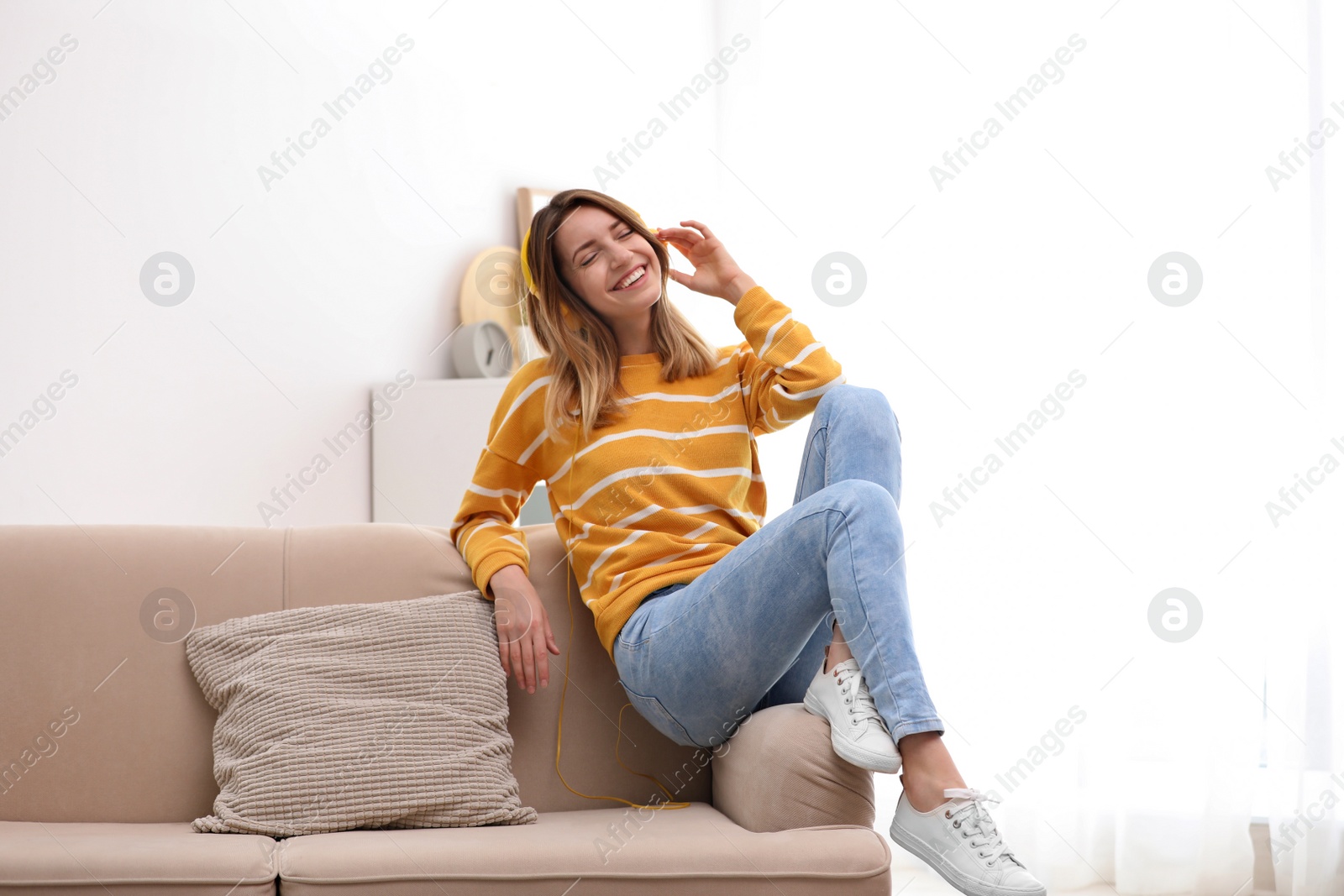 Photo of Young woman in headphones enjoying music on sofa at home