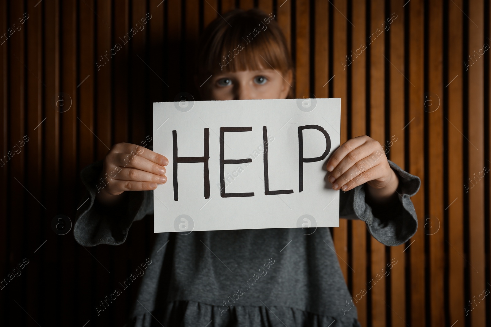 Photo of Sad little girl with sign HELP on wooden background. Child in danger