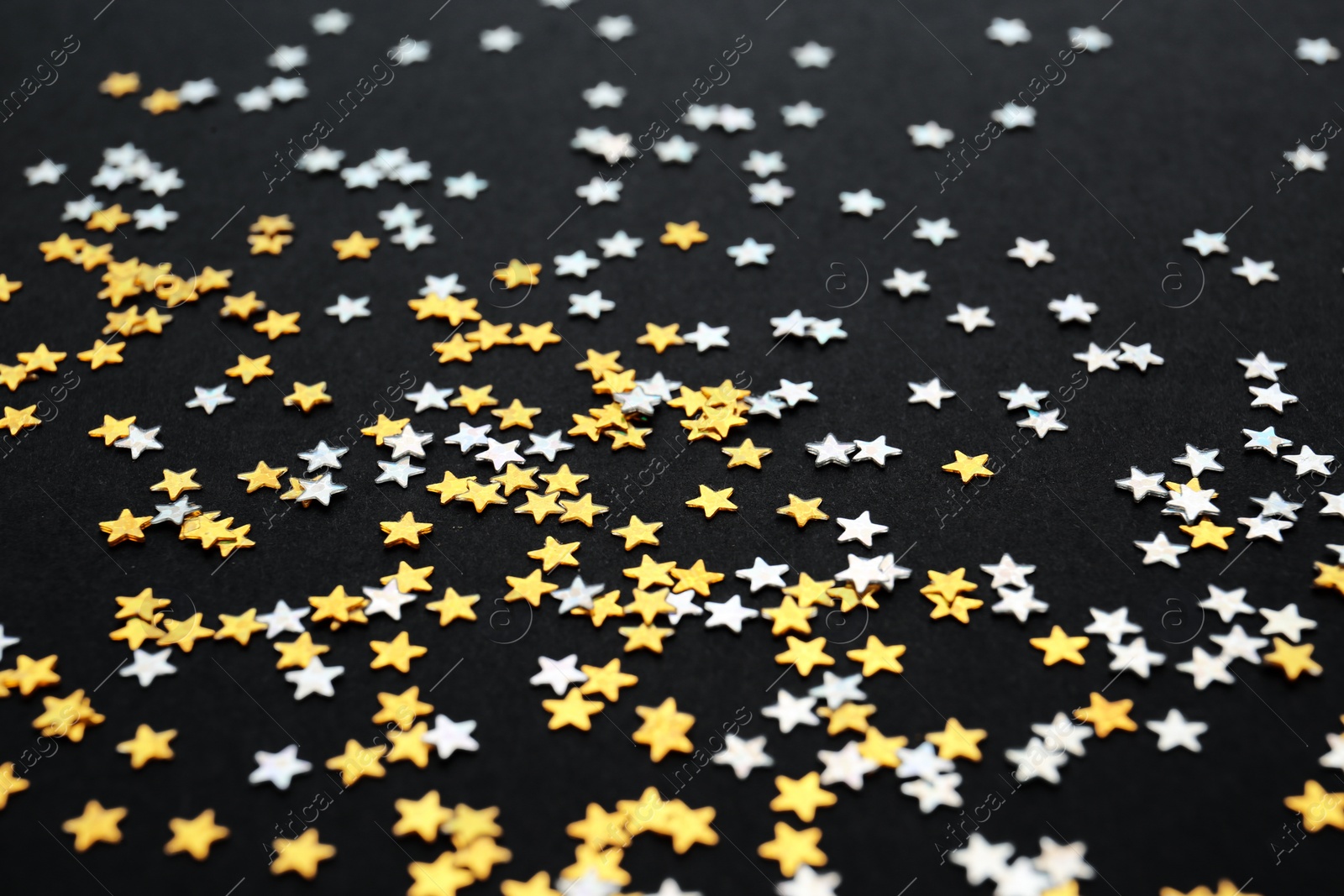 Photo of Gold and silver confetti stars on black background, closeup. Christmas celebration