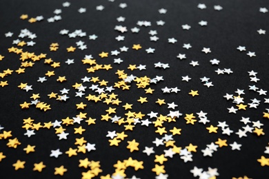 Photo of Gold and silver confetti stars on black background, closeup. Christmas celebration