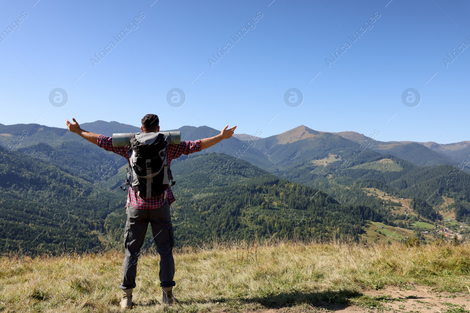 Photo of Happy man with backpack and camping mat in mountains on sunny day, back view