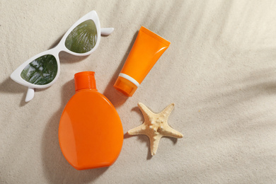 Sunglasses with reflection of palm trees and protection cosmetic products on sand, flat lay. Space for text